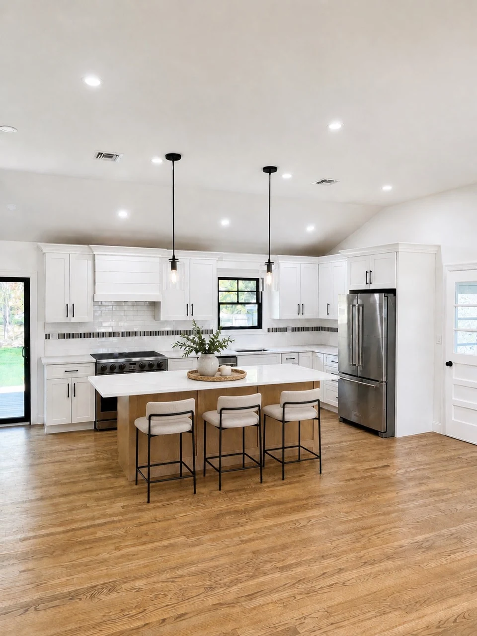 White kitchen with a warm wood island, three upholstered stools, and two pendant lights