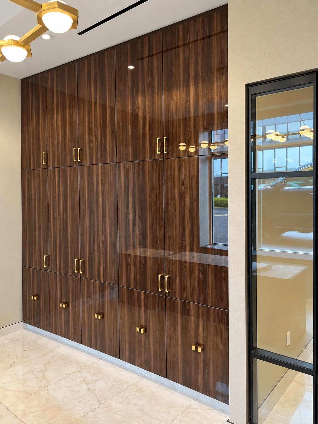 Floor-to-ceiling glossy dark wood office cabinetry with gold hardware